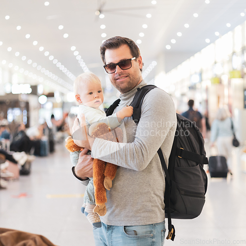 Image of Father traveling with child, holding his infant baby boy at airport terminal waiting to board a plane. Travel with kids concept.