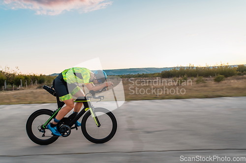 Image of Triathlete riding his bicycle during sunset, preparing for a marathon. The warm colors of the sky provide a beautiful backdrop for his determined and focused effort.