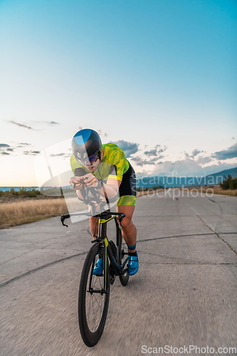 Image of Triathlete riding his bicycle during sunset, preparing for a marathon. The warm colors of the sky provide a beautiful backdrop for his determined and focused effort.