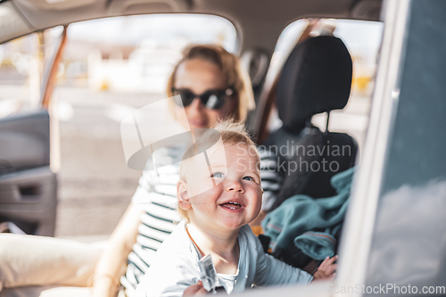 Image of Mother and her infant baby boy child on family summer travel road trip, sitting at dad's front seat, waiting in the car for father to buy farry tickets.