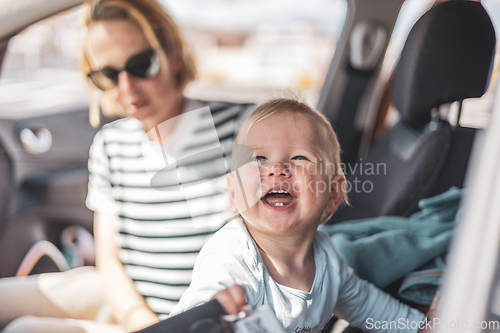 Image of Mother and her infant baby boy child on family summer travel road trip, sitting at dad's front seat, waiting in the car for father to buy farry tickets.