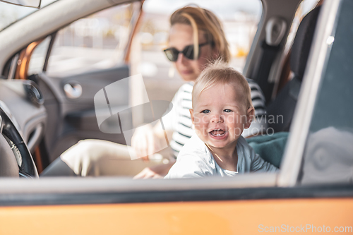 Image of Mother and her infant baby boy child on family summer travel road trip, sitting at dad's front seat, waiting in the car for father to buy farry tickets.
