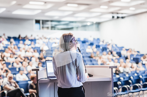 Image of Female speaker giving a talk on corporate business conference. Unrecognizable people in audience at conference hall. Business and Entrepreneurship event.