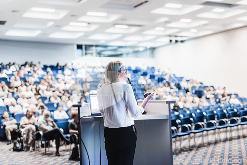 Image of Female speaker giving a talk on corporate business conference. Unrecognizable people in audience at conference hall. Business and Entrepreneurship event.