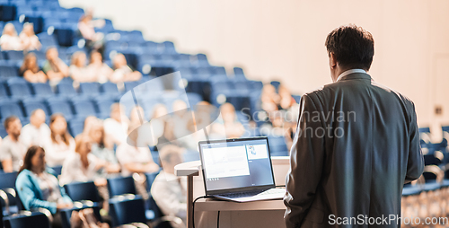 Image of Speaker giving a talk on corporate business conference. Unrecognizable people in audience at conference hall. Business and Entrepreneurship event.