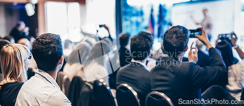 Image of Speaker giving a talk in conference hall at business event. Rear view of unrecognizable people in audience at the conference hall. Business and entrepreneurship concept.