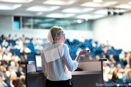 Image of Female speaker giving a talk on corporate business conference. Unrecognizable people in audience at conference hall. Business and Entrepreneurship event.