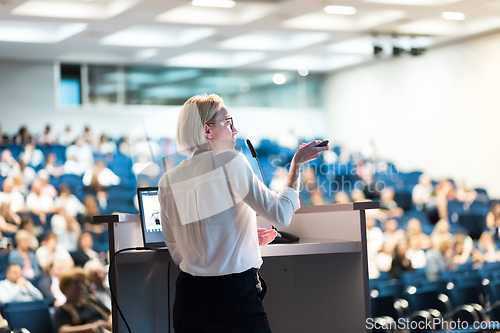 Image of Female speaker giving a talk on corporate business conference. Unrecognizable people in audience at conference hall. Business and Entrepreneurship event.