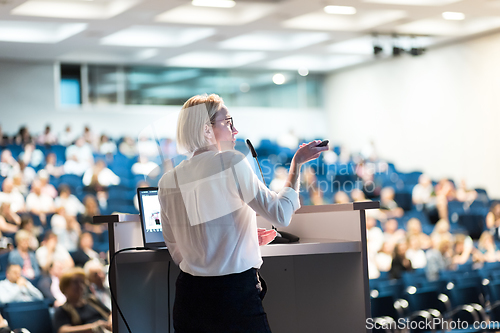 Image of Female speaker giving a talk on corporate business conference. Unrecognizable people in audience at conference hall. Business and Entrepreneurship event.