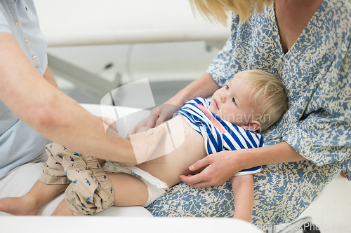 Image of Infant baby boy child being examined by his pediatrician doctor during a standard medical checkup in presence and comfort of his mother. National public health and childs care care koncept.