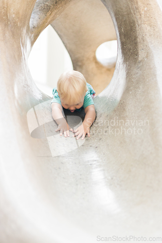 Image of Child playing on outdoor playground. Toddler plays on school or kindergarten yard. Active kid on stone sculpured slide. Healthy summer activity for children. Little boy climbing outdoors.