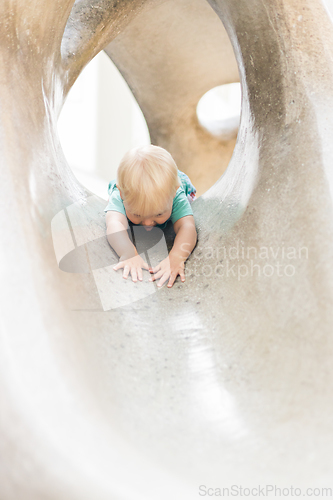 Image of Child playing on outdoor playground. Toddler plays on school or kindergarten yard. Active kid on stone sculpured slide. Healthy summer activity for children. Little boy climbing outdoors.