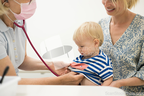 Image of Infant baby boy child being examined by his pediatrician doctor during a standard medical checkup in presence and comfort of his mother. National public health and childs care care koncept.