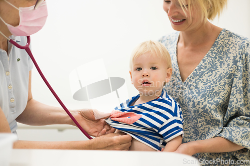 Image of Infant baby boy child being examined by his pediatrician doctor during a standard medical checkup in presence and comfort of his mother. National public health and childs care care koncept.