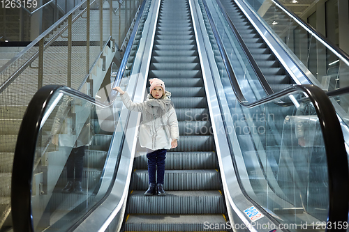 Image of From below shot of girl standing on moving stairs in terminal.