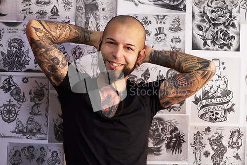 Image of Tattoos, creativity and portrait of a male artist standing by sketches or drawings in his studio. Happy, smile and face of a punk man with a edgy, funky and body art or ink creative business store.