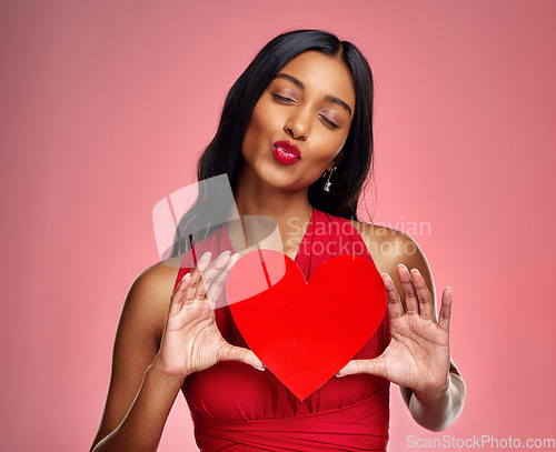 Image of Kiss, heart and valentines day with a woman on a pink background in studio for love or romance. Red lips, emoji and social media with a happy young female holding a shape or symbol of affection