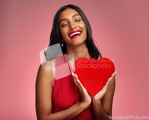 Image of Smile, heart and valentines day with a woman on a pink background in studio for love or romance. Eyes closed, emoji and social media with a happy young female holding a shape or symbol of affection