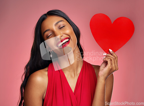 Image of Funny, heart and valentines day with a woman on a pink background in studio for love or romance. Smile, emoji and social media with a young female comic holding a shape or symbol of affection