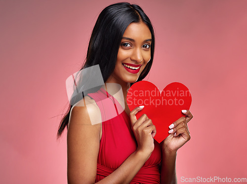 Image of Portrait, heart and valentines day with a woman on a pink background in studio for love or romance. Smile, emoji and social media with a happy young female holding a shape or symbol of affection