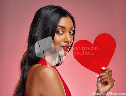 Image of Portrait, heart and love with a woman on a pink background in studio for romance on valentines day. Face, emoji and social media with a confident young female holding a shape or symbol of affection