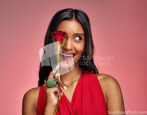 Image of Excited, beauty and face of a woman with a rose on a studio background for valentines day. Makeup, model and happy young Indian girl with a flower in hand for romance or love on pink backdrop