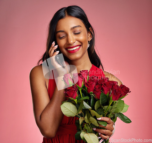 Image of Phone call, talking and a happy woman with flowers on a studio background for valentines day. Laugh, model and face of a young Indian girl with a rose bouquet and smartphone for romance or love