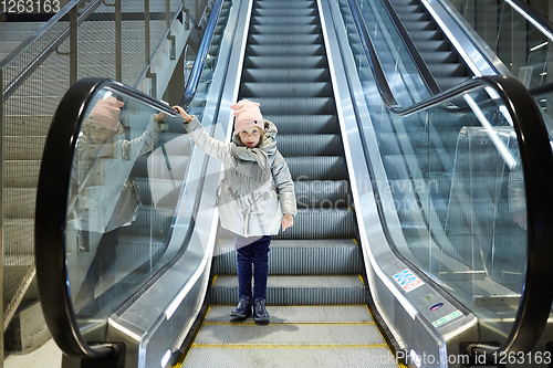 Image of From below shot of girl standing on moving stairs in terminal.