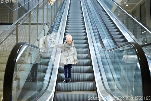 Image of From below shot of girl standing on moving stairs in terminal.