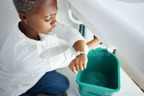 Image of Plumbing, leak and watch with a black woman in the bathroom of her home waiting for repair assistance. Sink, emergency and time with a young female homeowner in her house to stop water using a bucket