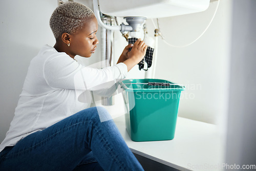 Image of Plumbing, leak and a black woman in the bathroom of her home with a cloth and bucket waiting for assistance. Sink, emergency and a burst pipe with a young female homeowner in her house to stop water