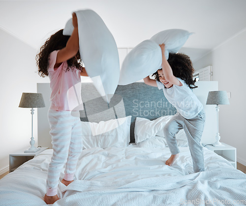 Image of Happy siblings, pillow fight and playing on bed in morning together for fun bonding at home. Little girls, children or kids enjoying playful game, entertainment or fighting with pillows in bedroom