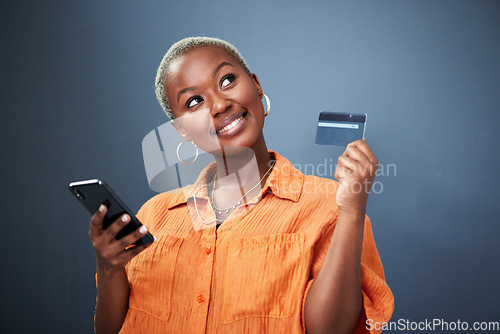 Image of Thinking, phone and credit card with a black woman online shopping in studio on a gray background. Mobile, ecommerce and finance payment with a young female shopper searching for a deal or sale