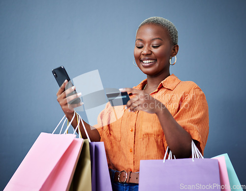 Image of Bags, retail and black woman with a credit card, smartphone or ecommerce on a grey studio background. Female person, shopper or model with cellphone, boutique items or purchase with shopping or smile