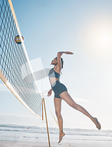 Image of Woman, jump and volleyball player on beach by net in serious sports match, game or competition. Fit, active and sporty female person jumping or reaching for ball in volley or spike by the ocean coast