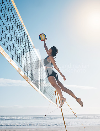 Image of Woman, jump and volleyball in air on beach by net in serious sports match, game or competition. Fit, active and sporty female person jumping or reaching for ball in volley or spike by the ocean coast