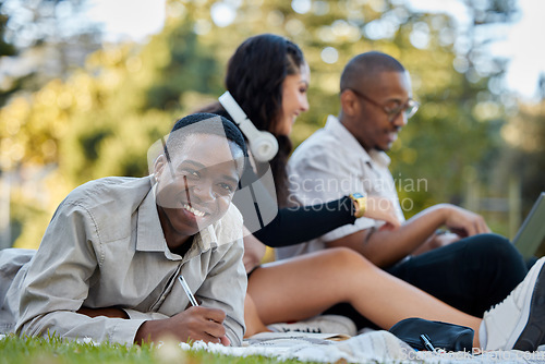 Image of Nature, university and portrait of a man studying on the grass with his friends for a test or exam. Happy, smile and African male student writing assignment in his notebook in park at college campus.