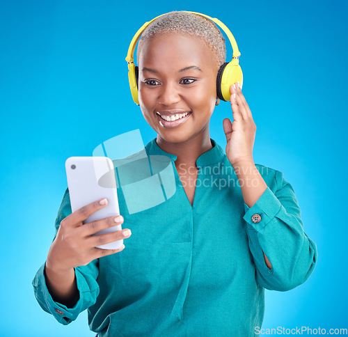 Image of Headphones, phone and woman listening on studio, blue background for podcast, music and streaming service. Mobile, audio technology and young african woman on electronics for radio, sound or hearing