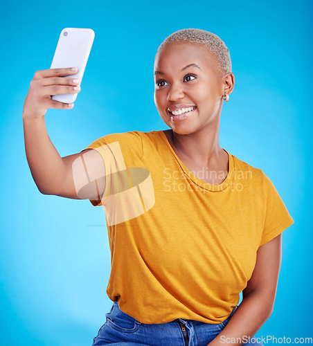 Image of Phone, selfie and smile with a black woman on a blue background in studio to update her status. Mobile, social media and a happy young female influencer taking a photograph for online profile