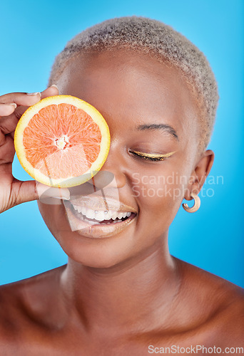 Image of Orange fruits, skincare and face of black woman in studio, blue background and eco makeup cosmetics. Beauty, happy female model and citrus for vitamin c, facial detox or healthy aesthetic dermatology