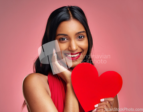 Image of Portrait, heart and romance with a woman on a pink background in studio for love or affection. Smile, emoji and social media with a happy young female holding a shape or symbol on valentines day