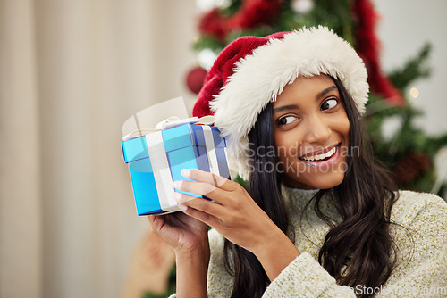 Image of Christmas, curious or happy woman with a gift or box in present on a holiday celebration at home. Guessing, smile or excited Indian girl with present with giveaway prize package in a house in winter