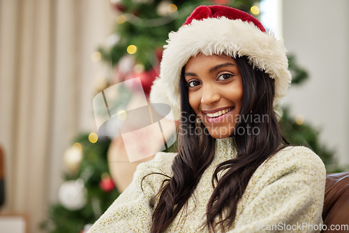 Image of Happy woman, portrait and Christmas on sofa by tree with hat for festive season, celebration or gift at home. Female person with smile in relax for holiday, weekend or December party at the house