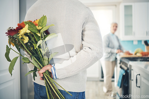 Image of Senior, couple and flowers for love in home, kitchen or husband with bouquet of roses to surprise woman in happy marriage. Man, wife and back hiding gift, flower and romance together on anniversary