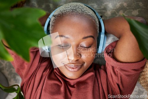 Image of Woman, face and headphones for listening to music to relax on a floor with plants for peace and calm. Headshot of a black female person meditate with sound, audio and podcast or radio at home