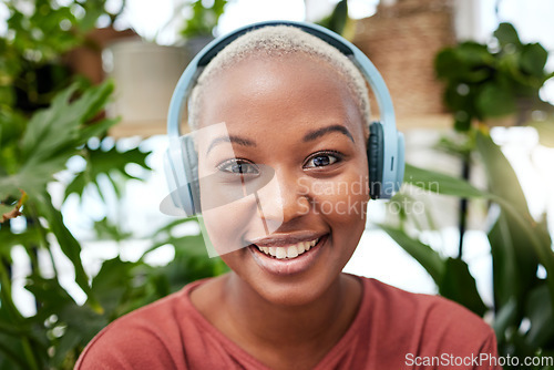 Image of Portrait, music and headphones with a black woman in her home by plants while streaming an audio playlist. Face, radio and subscription service with a carefree young female person in her house