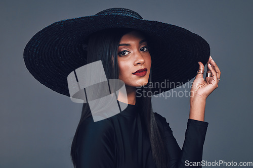 Image of Face, fashion and serious woman with hat in studio isolated on a gray background. Portrait, style and confident female model from India with makeup cosmetics, classy clothes and elegant aesthetic.