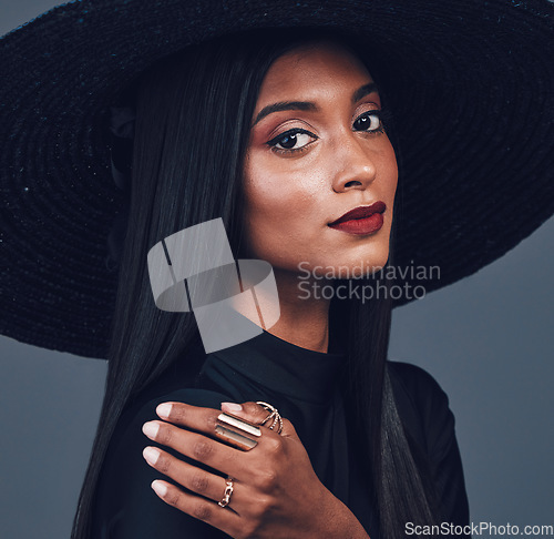 Image of Fashion, face and confident woman with hat in studio isolated on a gray background. Portrait, style and serious female model from India with makeup cosmetics, classy clothes and elegant aesthetic.