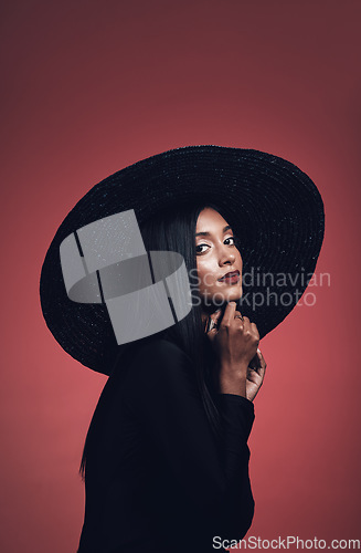 Image of Portrait, fashion and confident woman with hat in studio isolated on red background mockup space. Face, style and serious model from India with makeup cosmetics, classy clothes and elegant aesthetic.