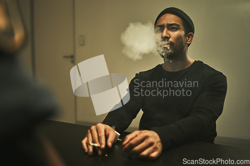 Image of Man in handcuffs, smoking and talking to detective in interrogation room with criminal, suspect or interview with a gangster. Police officer, questioning in arrest and person in investigation